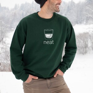 Pode incluir: Uma camisa de frio verde escura com um gr&aacute;fico branco de um copo de &aacute;gua e a palavra "neat" impressa na frente.