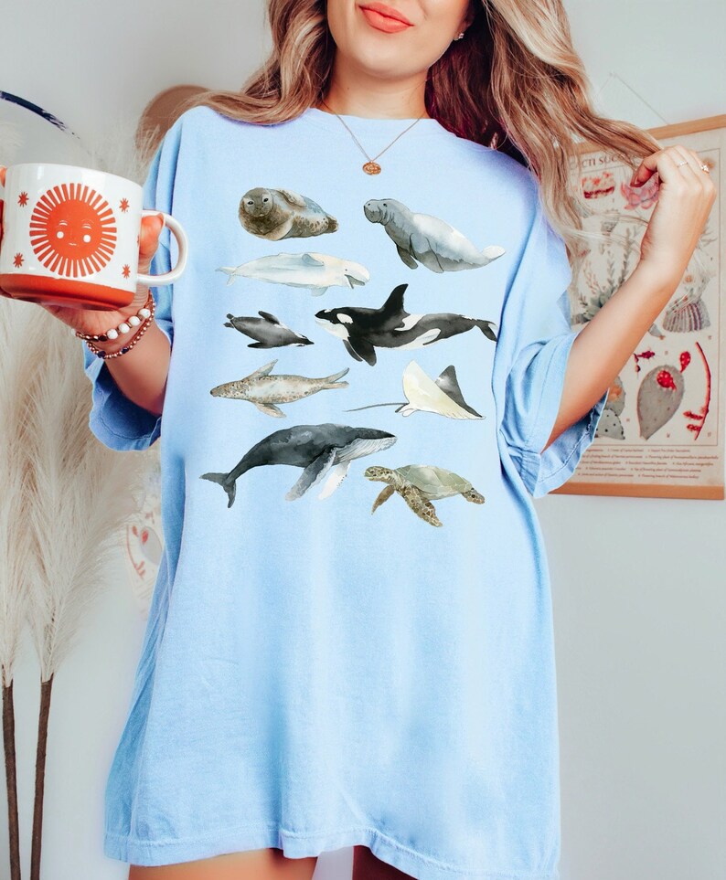May include: A light blue t-shirt with a watercolor illustration of various sea creatures, including a whale, dolphin, sea turtle, and stingray.