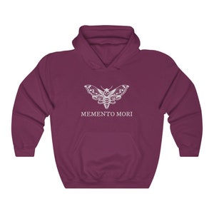 K&ouml;nnte beinhalten: Ein maroonfarbener Kapuzenpullover mit einem wei&szlig;en Motiv eines Motten mit einem Totenkopf auf dem Kopf und dem Text "MEMENTO MORI" darunter.