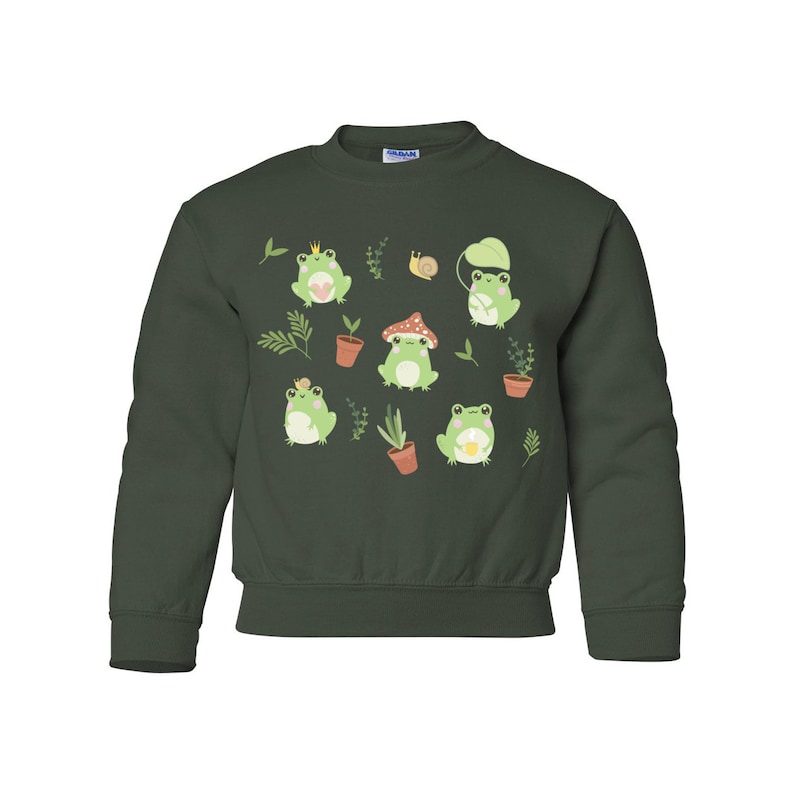 K&ouml;nnte beinhalten: Ein dunkelgr&uuml;ner Pullover mit einem Muster aus gr&uuml;nen Fr&ouml;schen, Pflanzen und Pilzen. Die Fr&ouml;sche tragen Kronen und halten Blumen.