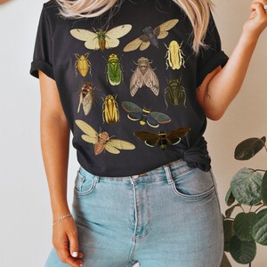 May include: A black t-shirt featuring a graphic print of various insects, including butterflies, beetles, and cicadas. The insects are depicted in a vintage style with detailed illustrations.