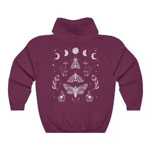 Pu&ograve; includere: Una felpa con cappuccio color granata con un design grafico bianco che presenta una falena, funghi e lune. Il design &egrave; centrato sulla felpa.