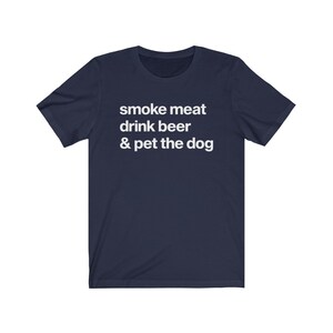 K&ouml;nnte beinhalten: Ein marineblaues T-Shirt mit wei&szlig;em Text, der "smoke meat drink beer & pet the dog" lautet.