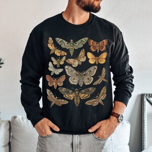 K&ouml;nnte beinhalten: Schwarzes Sweatshirt mit einer Vintage-Illustration verschiedener Motten und Schmetterlinge in Braun-, Gr&uuml;n-, Gelb- und Wei&szlig;t&ouml;nen.