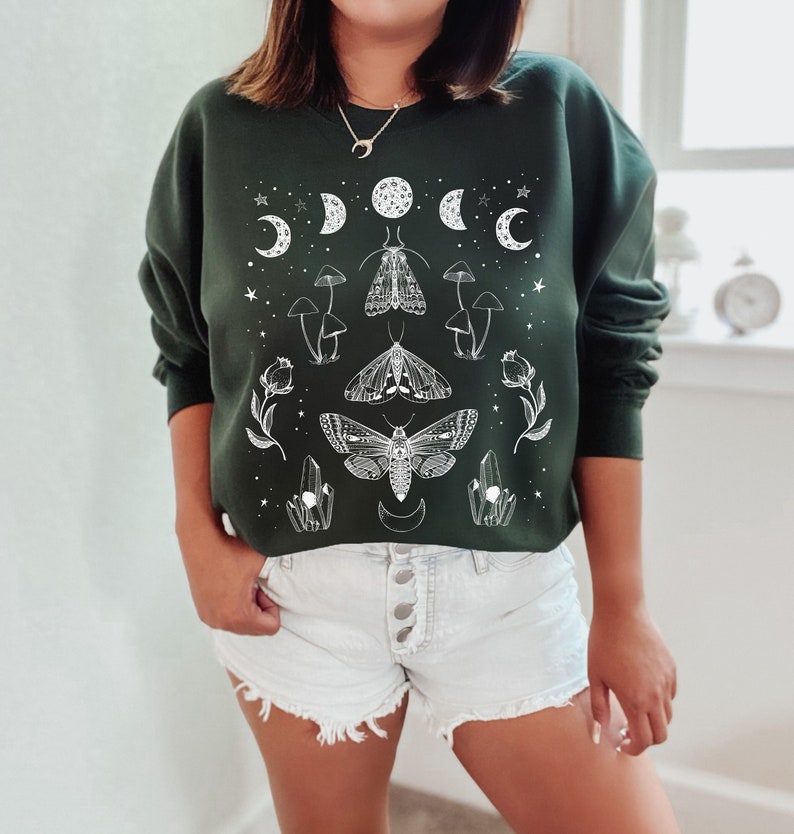 May include: A dark green sweatshirt with a white graphic print of moths, mushrooms, crystals, and crescent moons.