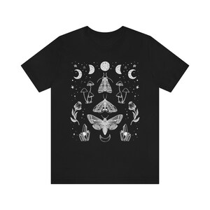 Puede incluir: Camiseta negra con un dise&ntilde;o gr&aacute;fico blanco con polillas, hongos, cristales y lunas.