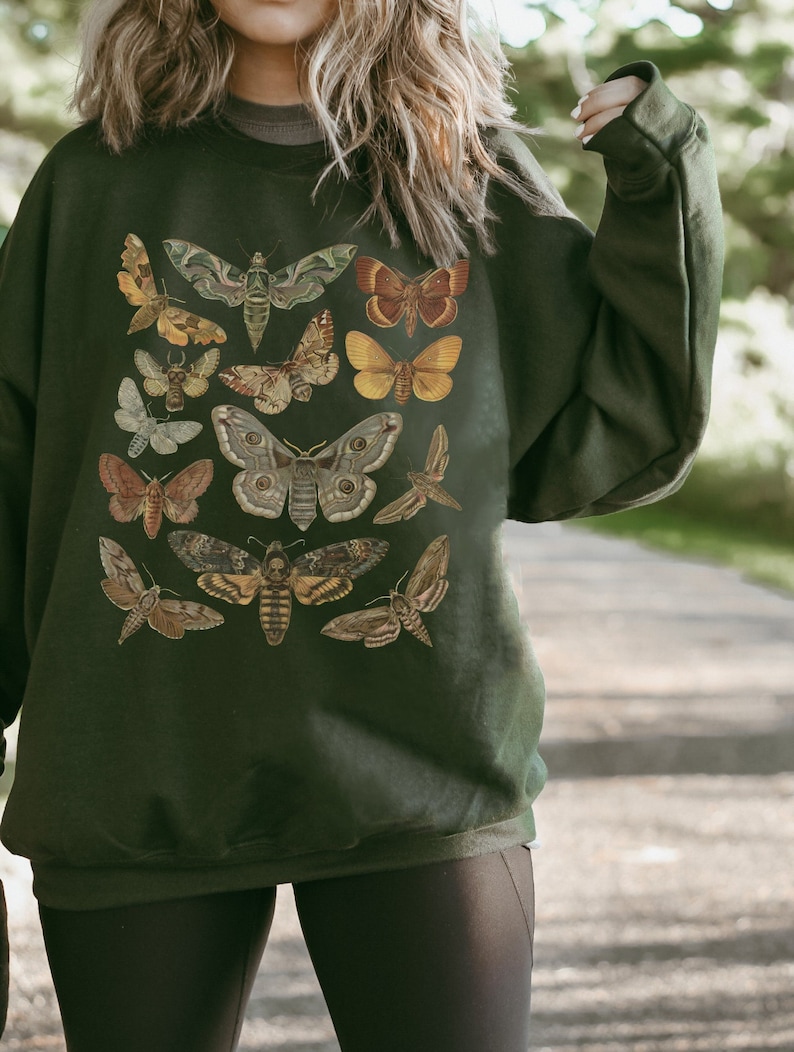 K&ouml;nnte beinhalten: Ein dunkelgr&uuml;ner Pullover mit einer Vintage-Illustration verschiedener Motten und Schmetterlinge in Braun-, Gelb- und Wei&szlig;t&ouml;nen.
