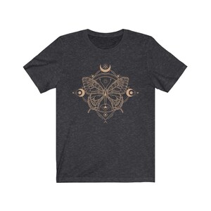 May include: A dark heather grey t-shirt with a graphic of a butterfly inside a geometric design. The butterfly is a light brown color and the geometric design is a light gold color.