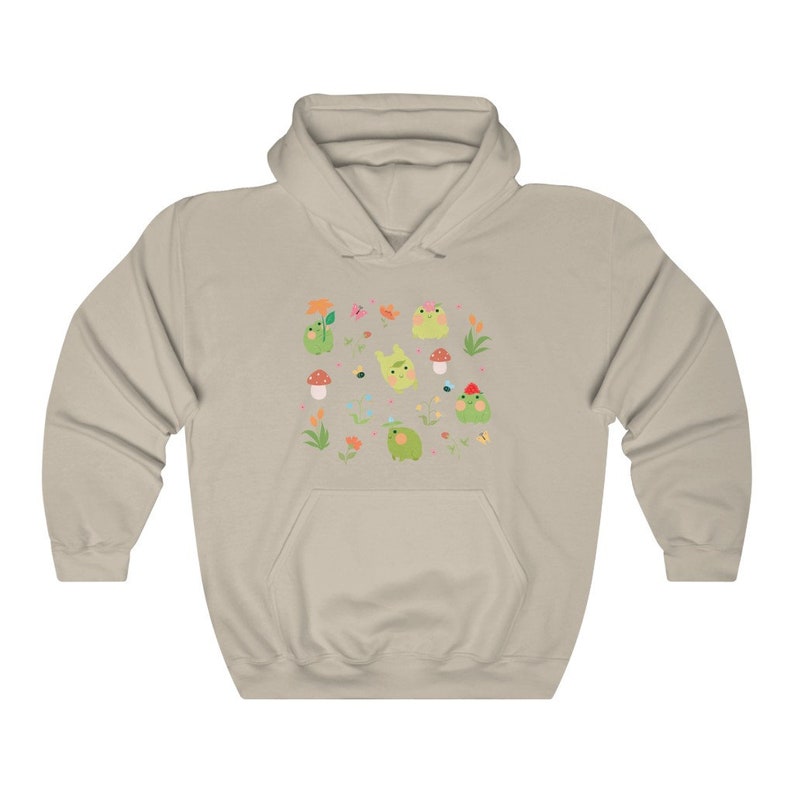 May include: A light beige hoodie with a print of green frogs, flowers, and mushrooms. The print is a repeating pattern and covers the entire front of the hoodie.