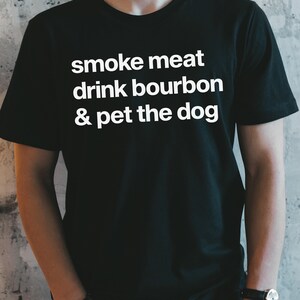 May include: A black t-shirt with white text that reads "smoke meat drink bourbon & pet the dog".