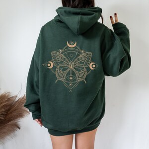 May include: A dark green hooded sweatshirt with a graphic print of a butterfly with geometric shapes and crescent moons in a light brown color.