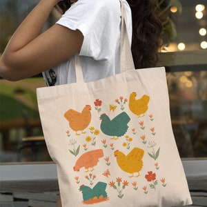May include: A beige tote bag with a colorful illustration of chickens and flowers. The chickens are in various colors, including orange, yellow, green, and blue. The flowers are in shades of pink, red, and orange.