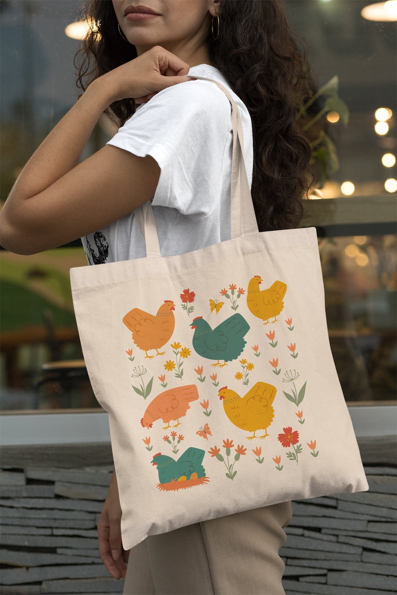 May include: A beige tote bag with a colorful illustration of chickens and flowers. The chickens are in various colors, including orange, yellow, green, and blue. The flowers are in shades of pink, red, and orange.