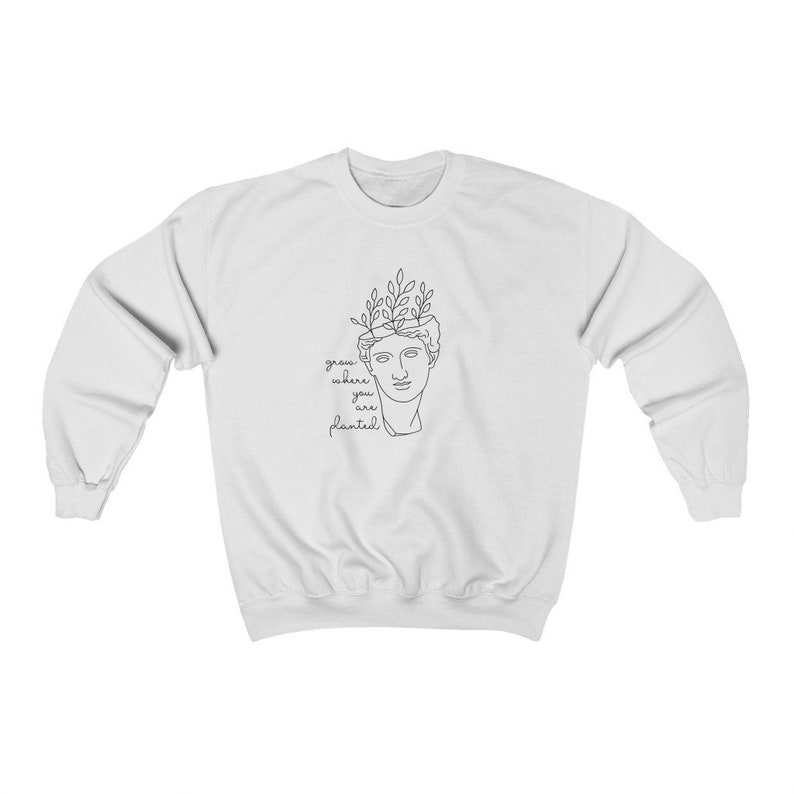 May include: White sweatshirt with a black line drawing of a bust with plants growing out of the top. The text "grow where you are planted" is below the drawing.
