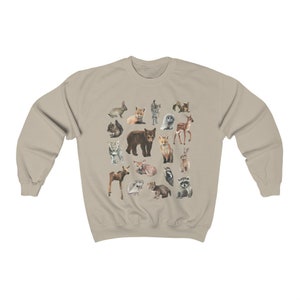 May include: A beige sweatshirt featuring a colourful print of various woodland animals, including a bear, fox, deer, rabbit, owl and raccoon.