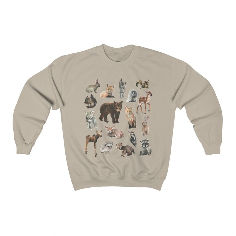 May include: A beige sweatshirt featuring a colourful print of various woodland animals, including a bear, fox, deer, rabbit, owl and raccoon.