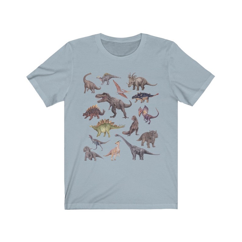 May include: A light blue t-shirt with a colorful illustration of various dinosaurs. The dinosaurs are depicted in a watercolor style and include a variety of species, such as a Tyrannosaurus Rex, a Triceratops, and a Stegosaurus.