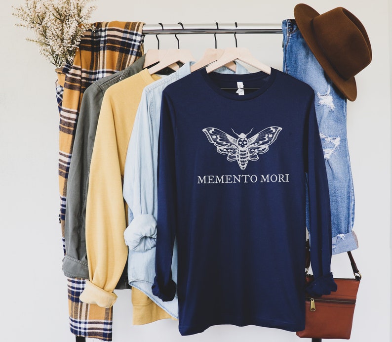 May include: Navy blue long-sleeved shirt with a white moth graphic and the text "Memento Mori".