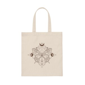 May include: A beige tote bag with a brown butterfly design. The butterfly is surrounded by a geometric pattern with crescent moons.