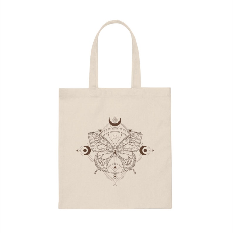 May include: A beige tote bag with a brown butterfly design. The butterfly is surrounded by a geometric pattern with crescent moons.