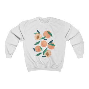 K&ouml;nnte beinhalten: Wei&szlig;er Pullover mit einem Grafikdruck von Pfirsichen mit gr&uuml;nen Bl&auml;ttern.