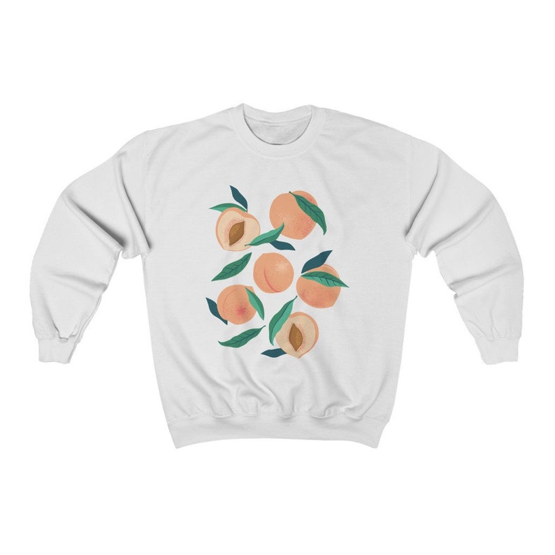 K&ouml;nnte beinhalten: Wei&szlig;er Pullover mit einem Grafikdruck von Pfirsichen mit gr&uuml;nen Bl&auml;ttern.