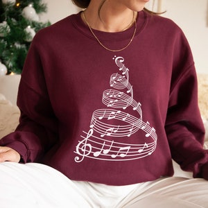 May include: A maroon sweatshirt with a white design of a Christmas tree made of musical notes.