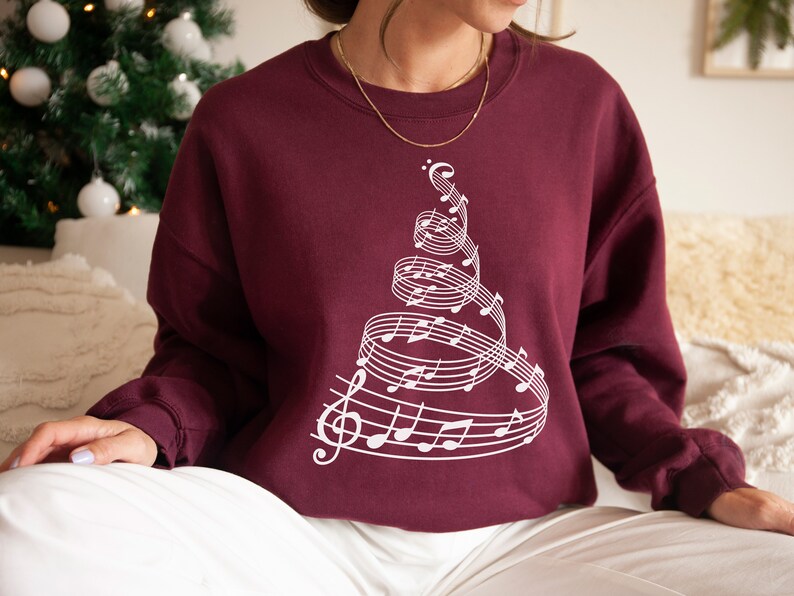 May include: A maroon sweatshirt with a white design of a Christmas tree made of musical notes.