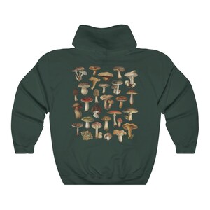 May include: Dark green hoodie featuring a collection of various mushroom illustrations in shades of brown, red, and beige. The mushrooms are arranged in a cluster on the back of the hoodie. The hoodie has a hood and long sleeves.