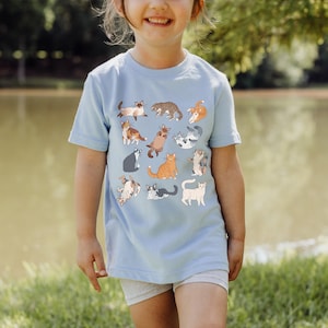 May include: A light blue t-shirt with a pattern of 12 colorful cats in various poses. The shirt is made of a soft, comfortable material.