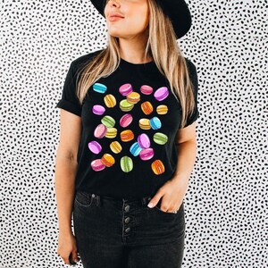 May include: A black t-shirt with a colorful macaron pattern. The macarons are pink, green, yellow, and blue.