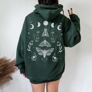 May include: A dark green hooded sweatshirt with a white graphic print of moths, mushrooms, crystals, and moons.