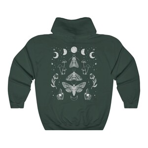 Pu&ograve; includere: Una felpa con cappuccio verde scuro con una stampa grafica bianca di falene, funghi, cristalli e lune.