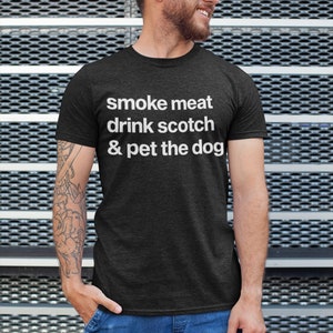 May include: A dark grey t-shirt with white text that reads "smoke meat drink scotch & pet the dog".