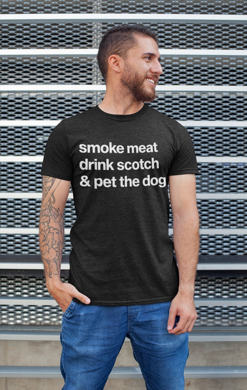 May include: A dark grey t-shirt with white text that reads "smoke meat drink scotch & pet the dog".