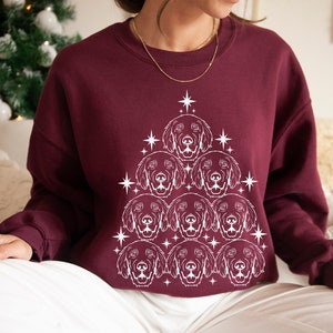 May include: A maroon sweatshirt with a white outline of a Christmas tree made of dog faces. The tree is decorated with stars.