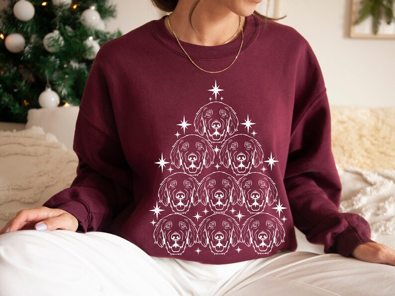 May include: A maroon sweatshirt with a white outline of a Christmas tree made of dog faces. The tree is decorated with stars.