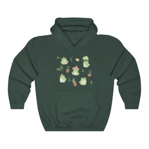 May include: A dark green hoodie with a pattern of frogs, mushrooms, and plants. The frogs are wearing crowns, hats, and holding flowers.