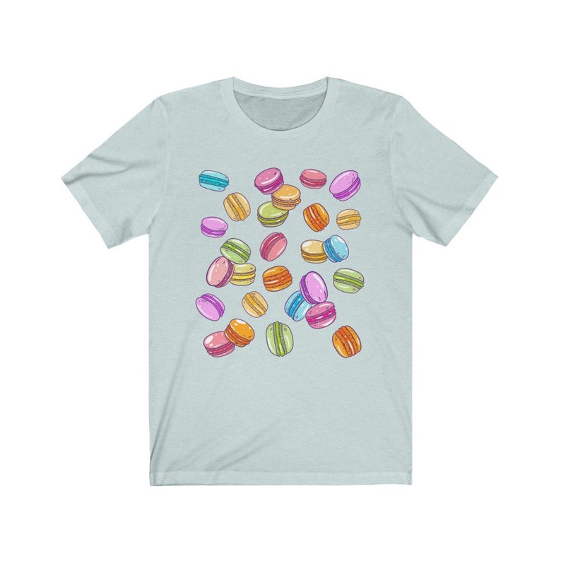 May include: A light blue t-shirt with a pattern of colorful macarons. The macarons are scattered randomly across the shirt.