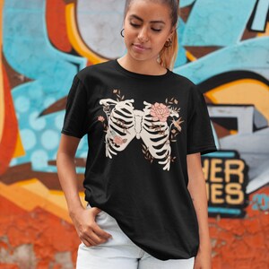 May include: Black t-shirt with a floral skeleton design. The skeleton is surrounded by flowers and leaves in shades of pink and green.