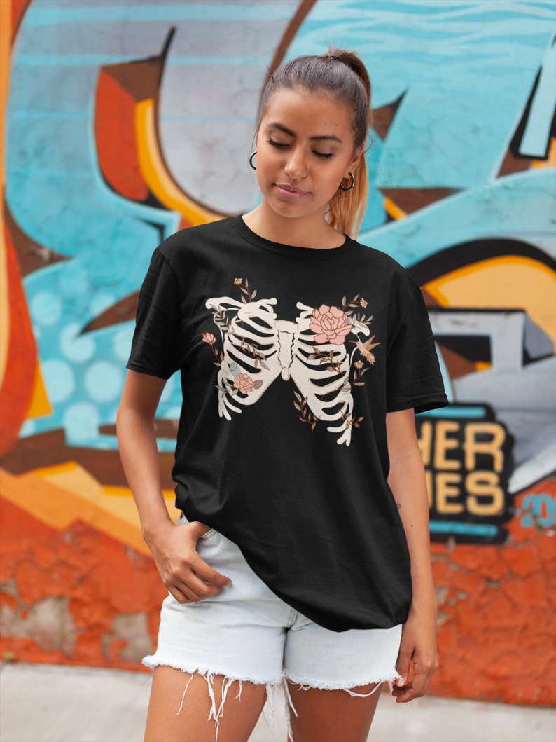 May include: Black t-shirt with a floral skeleton design. The skeleton is surrounded by flowers and leaves in shades of pink and green.