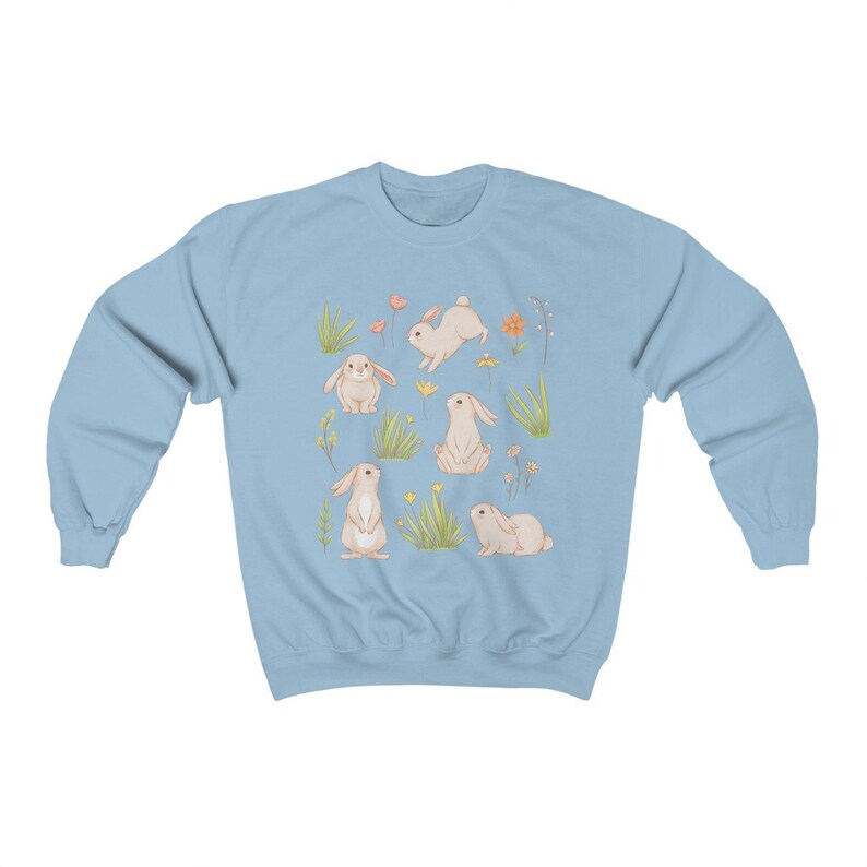May include: A light blue sweatshirt with a pattern of white bunnies and flowers. The bunnies are in various poses, including sitting, standing, and hopping. The flowers are in shades of pink, orange, and yellow.