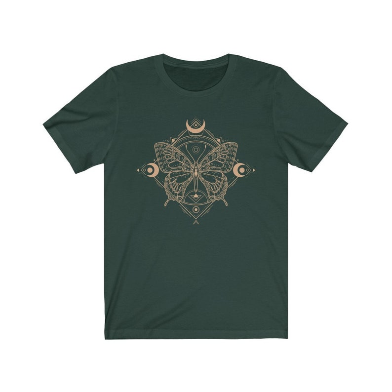 May include: A dark green t-shirt with a beige butterfly graphic. The butterfly is surrounded by a geometric design with crescent moons and other shapes.