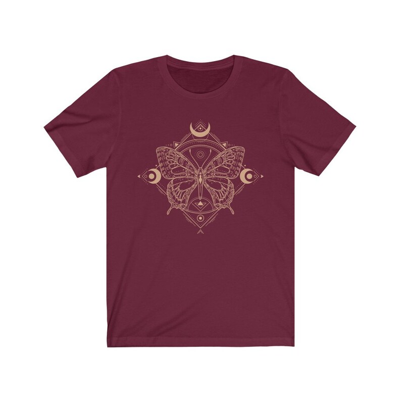 May include: A maroon t-shirt with a gold geometric design featuring a butterfly and crescent moons.