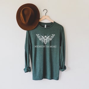 May include: A dark green long-sleeved shirt with a white moth graphic and the text "MEMENTO MORI" printed on the front.