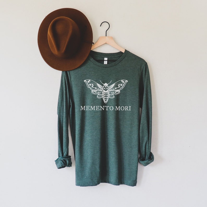 May include: A dark green long-sleeved shirt with a white moth graphic and the text "MEMENTO MORI" printed on the front.