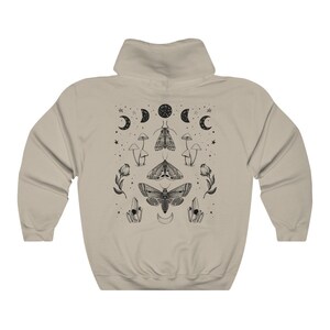 Pu&ograve; includere: Una felpa con cappuccio beige con una stampa grafica in bianco e nero di falene, funghi e lune. La grafica &egrave; centrata sul retro della felpa con cappuccio.