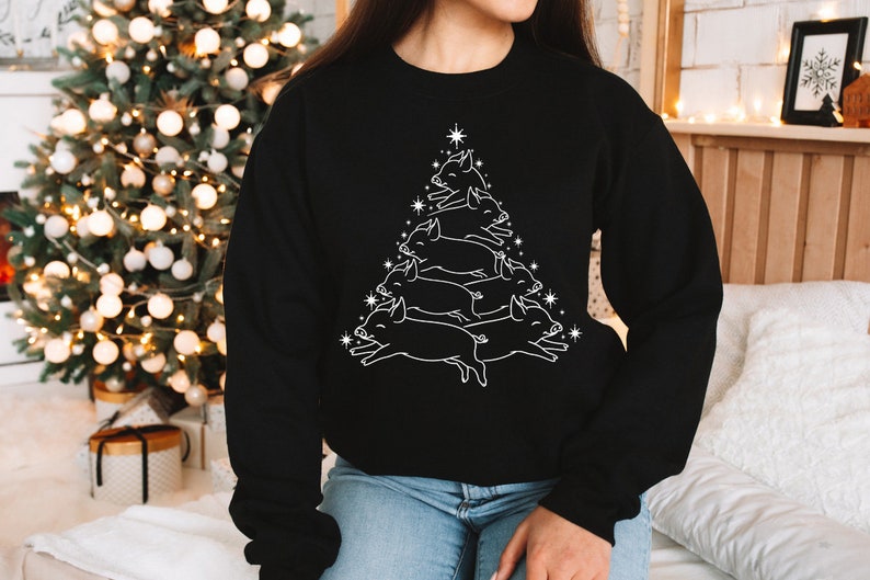 May include: A black sweatshirt featuring a white outline of a Christmas tree formed by stacked pigs. The pigs are arranged in a pyramid shape.