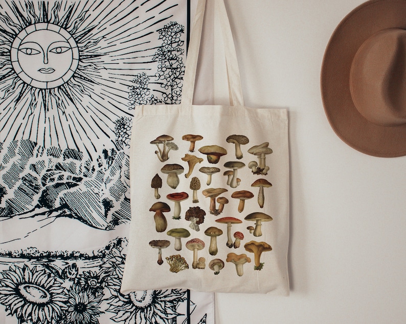 May include: A white canvas tote bag with a design of various mushrooms in shades of brown, red, and white. The mushrooms are arranged in a grid pattern on the bag.