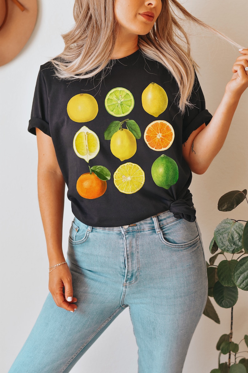 Pode incluir: Uma camiseta preta com uma estampa gr&aacute;fica de v&aacute;rias frutas c&iacute;tricas, incluindo lim&otilde;es, limas, laranjas e toranjas. As frutas est&atilde;o dispostas em uma grade na camiseta.
